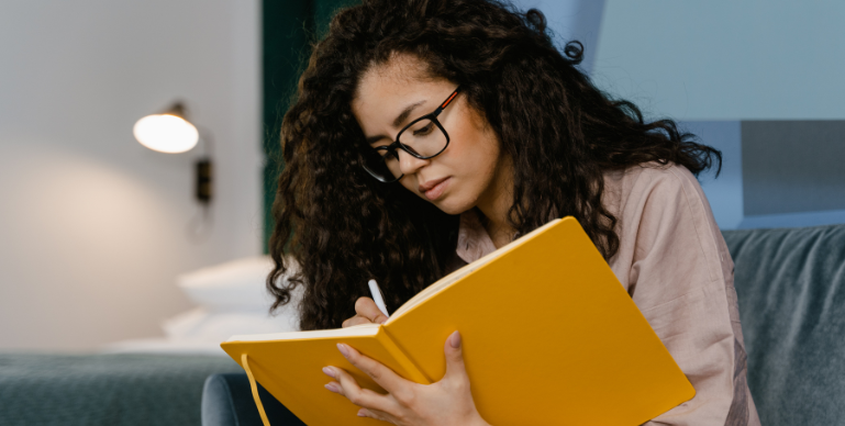 young woman writing in a journal she is holding with her other hand