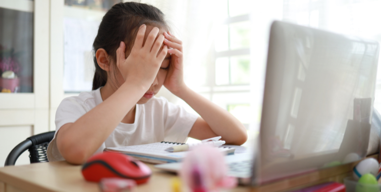 young asian youth covering her face with her hands while sitting in front of a computer