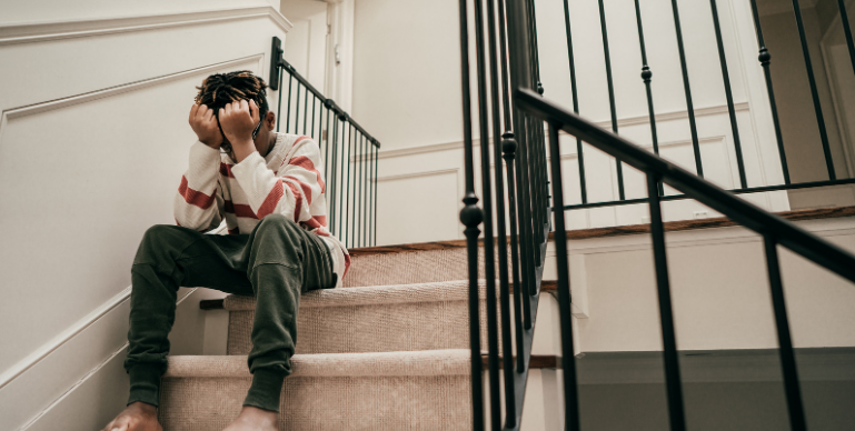 black teenager sitting on the steps of an outdoor porch with his forehead against his fists