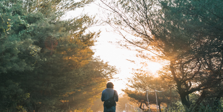 social anxiety treatment - a young man walks in the middle of the road into the dawn surrounded on either side by trees