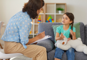 finding the best child psychologist is a hard task, let us help - child speaks to a woman with a clipboard and pen who is listening intently