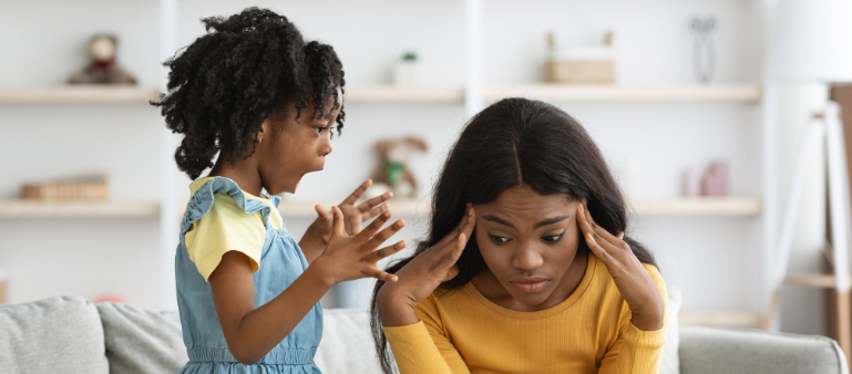 a mother sits with her hands to her head, while her daughter stands beside her talking in an animated way with her hand (adhd types)