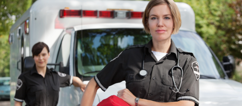 a female paramedic faces forward smiling with an ambulance in the background (benefits of therapy for first responders)