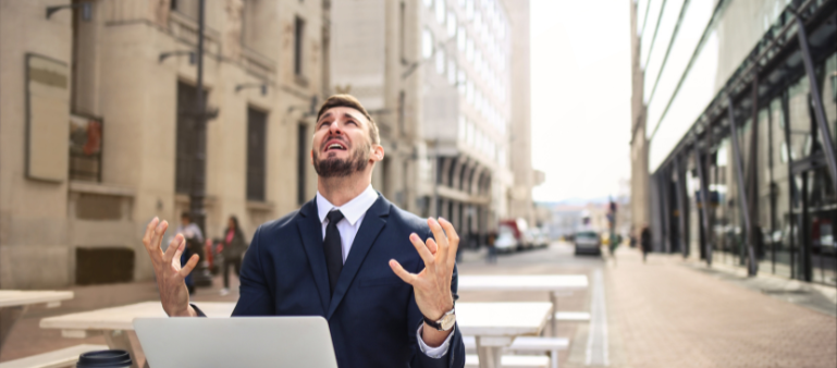 man at a desk on an empty urban street looking up and putting his hands up in frustration (signs and symptoms of anxiety in high performers)