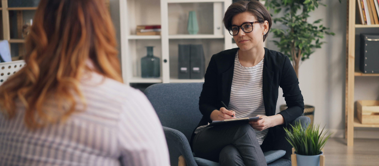 picture of a woman sitting with a clipboard with a sympathetic look facing another woman